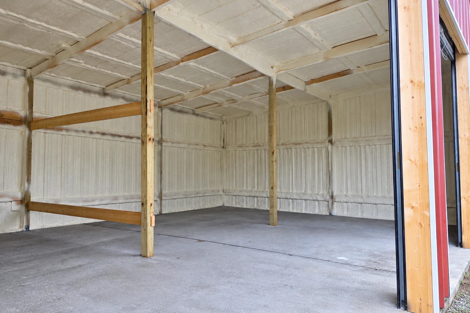 A large commercial space has white spray foam insulation covering its walls and ceiling above a concrete floor.