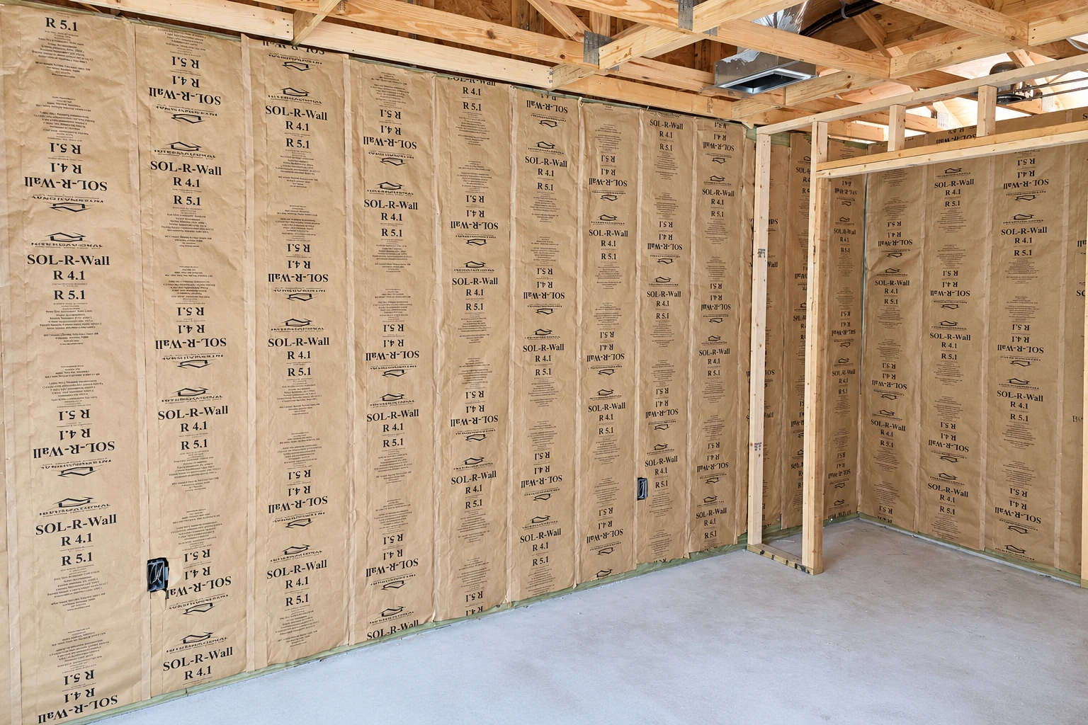 Paper-faced fiberglass insulation is fitted between the exposed wall studs in a bare commercial interior.