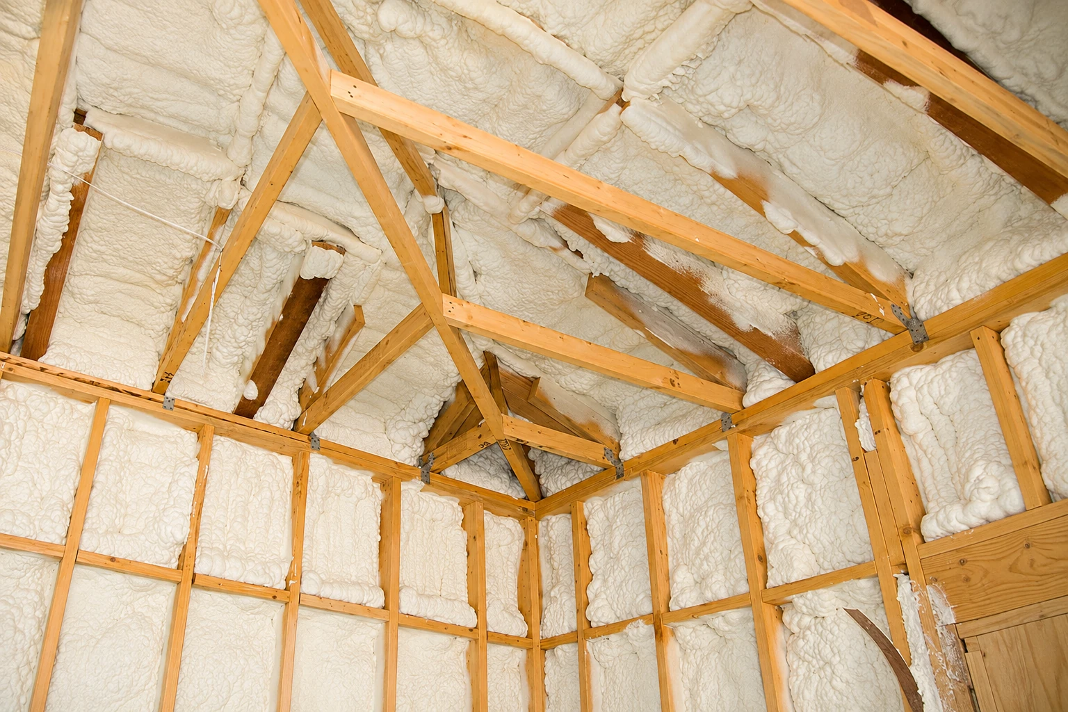 Wood-framed attic walls and rafters are densely filled with white spray foam insulation.